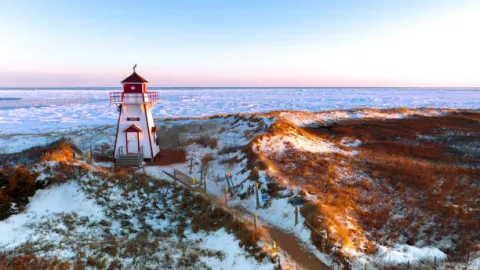 Lighthouse overlooking rocky coastline with light snow on ground.